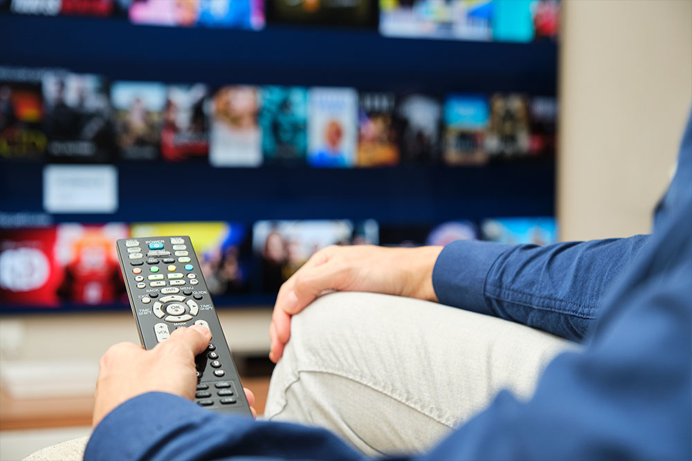 A man sitting on the sofa with a remote control in his hand searching for content on a streaming platform